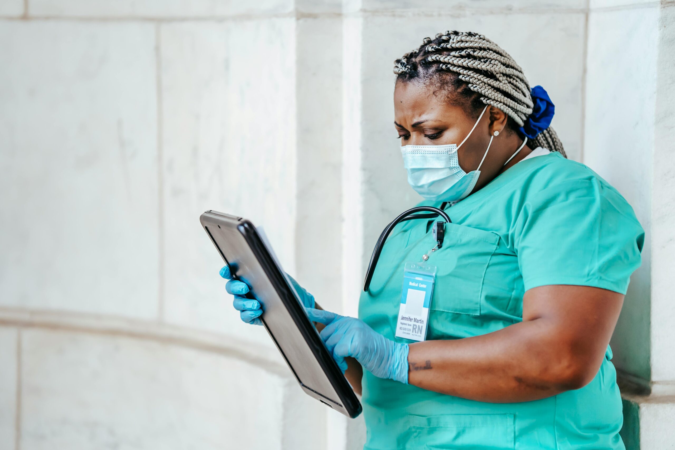 Focused middle aged ethnic female medic in uniform with clipboard and Afro braids in daylight